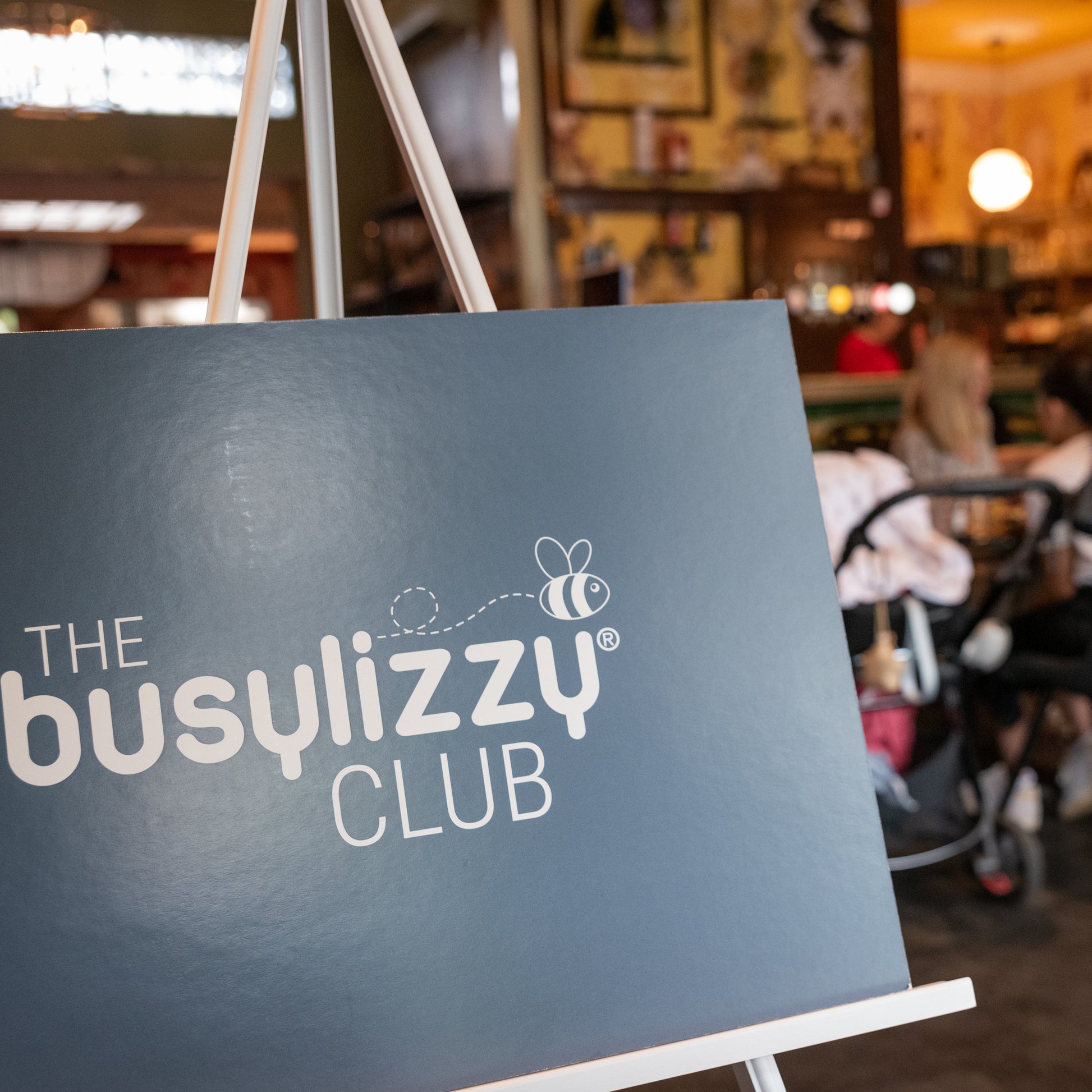 Blue sign with 'The Busylizzy Club' logo in a casual dining setting