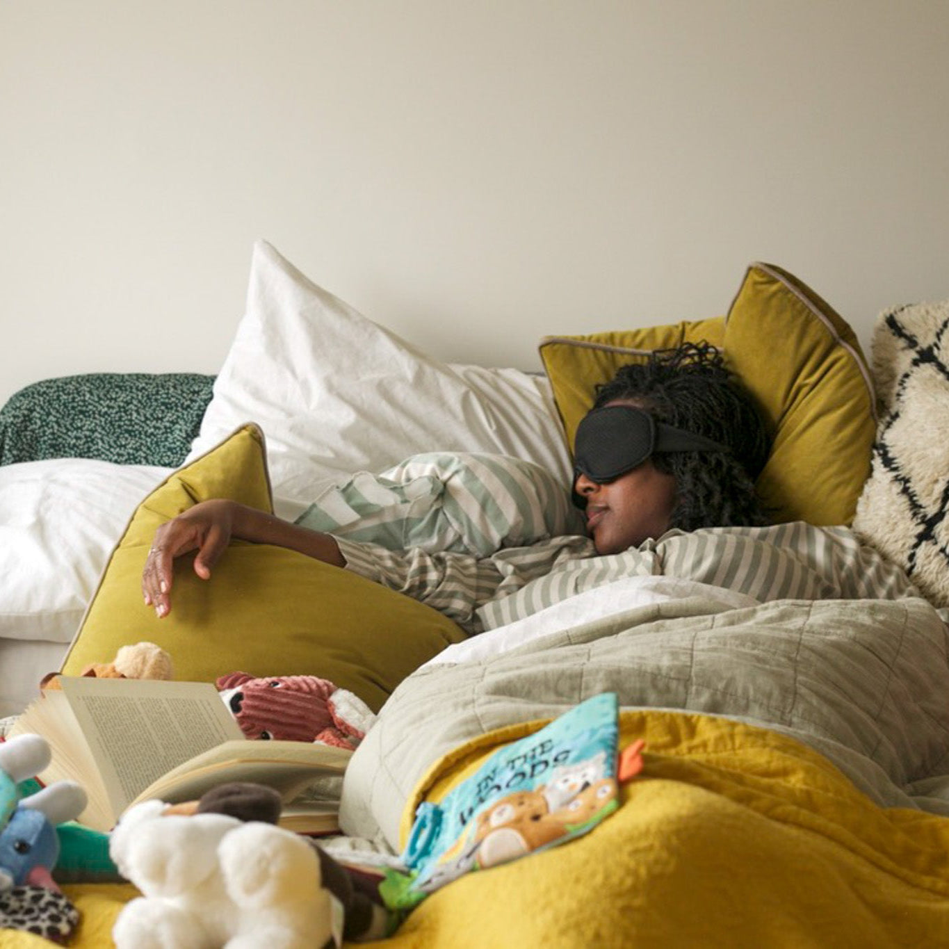 Person lying on a bed with pillows and blankets, wearing a sleep mask.