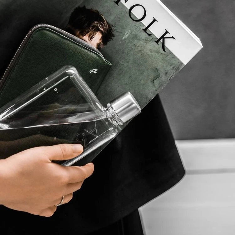Person holding a clear water bottle in a flat shape, with a magazine titled 'Kinfolk' in the background